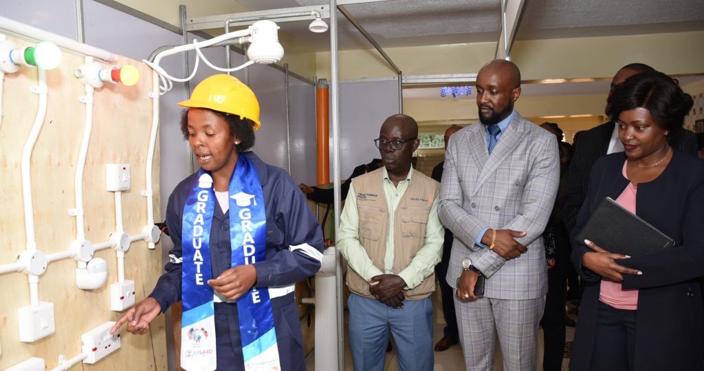  USAID Tumikia Mtoto Project electrical beneficiary Jackline Wanjiku demonstrates to World Vision Kenya National Director Gibert Kamanga, Kasarani MP Hon. Ronald Karauri & Family Bank CEO Rebecca Mbithi during the graduation ceremony of 100 young women trained in vocational and technical skills where the Bank doubled the investment to provide technical skills training to 2000 youth.